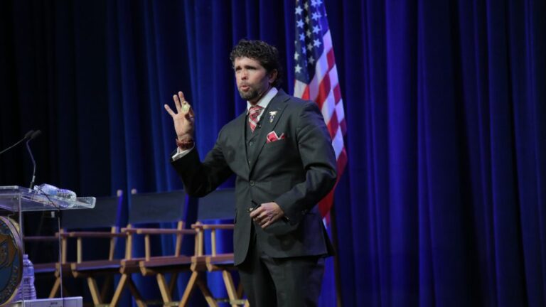 Jason Redman at podium with American flag backdrop presenting to audience, demonstrating confident public speaking and professional presentation techniques