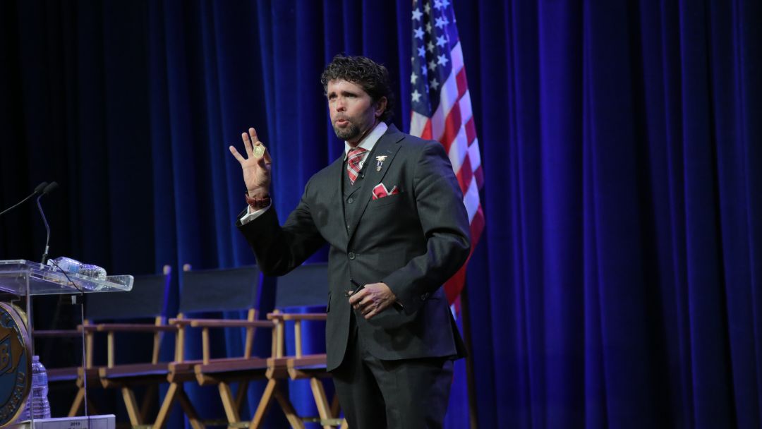 Jason Redman at podium with American flag backdrop presenting to audience, demonstrating confident public speaking and professional presentation techniques