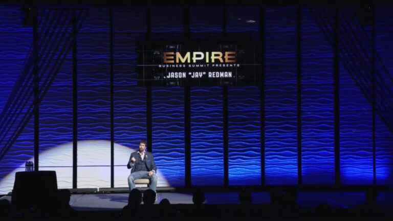 Professional speaker on stage at Empire Business Summit with blue backdrop and audience, illustrating motivational speaking expertise