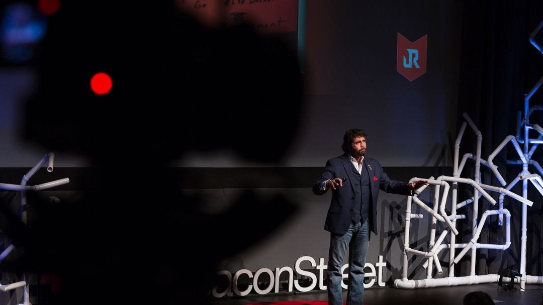 Dynamic keynote speaker on a TEDx-style stage with dramatic lighting and an engaged audience, illustrating the real impact a keynote speaker can make.