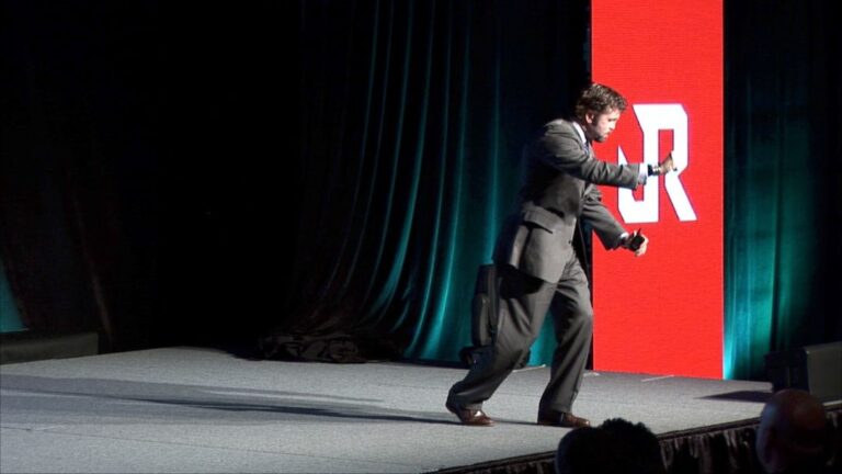 Jason Redman delivering an energetic performance on a corporate event stage, illustrating the dynamic difference between a motivational and keynote speaker.
