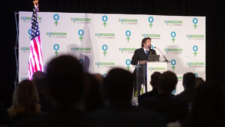 Keynote speaker presenting at a formal Concussion Legacy Foundation event before a seated audience, illustrating how different speaker types suit different event formats.