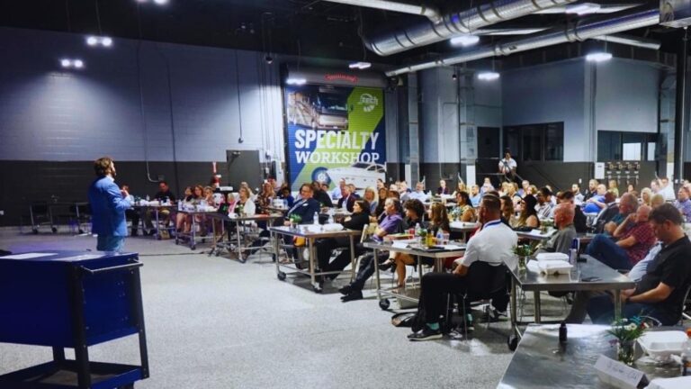 Professional speaker addressing full specialty workshop audience in industrial venue — hire a speaker vs in-house presenter and what top companies actually do.